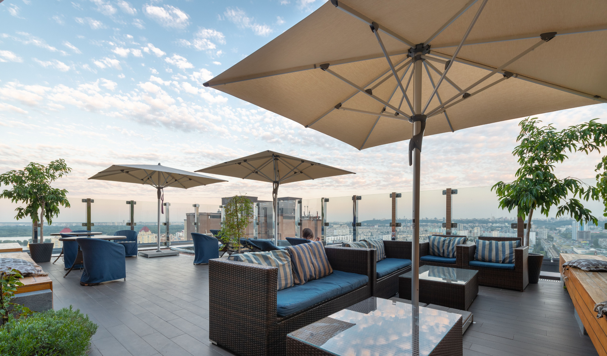 Outdoor rooftop lounge with furniture and umbrellas overlooking a cityscape.